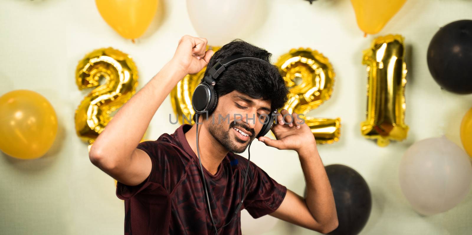 Young man enjoying by listining music on headset over 2021 new year decorated background - concept of solo new year partying or celebration due to coronavirus pandemic