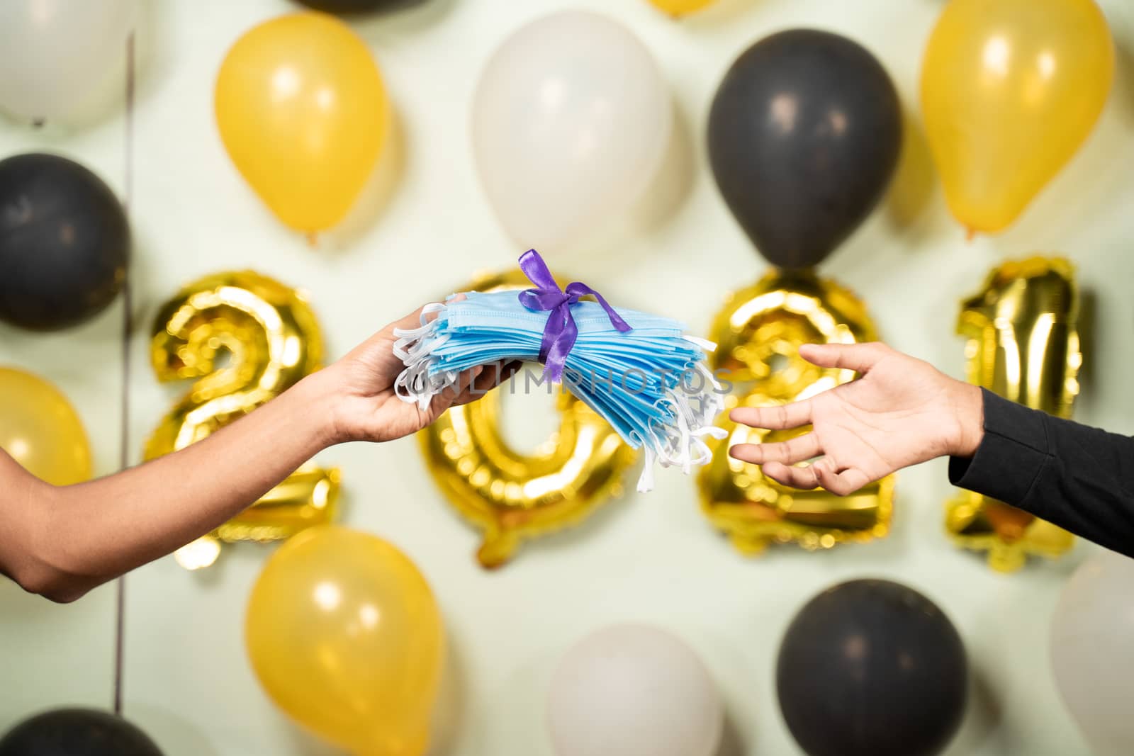 Close up of hands giving present gift as Medical face mask in 2021 new year decorated background - Concept of gift sharing on new year holydays during coronavirus or covid-19 pandemic.