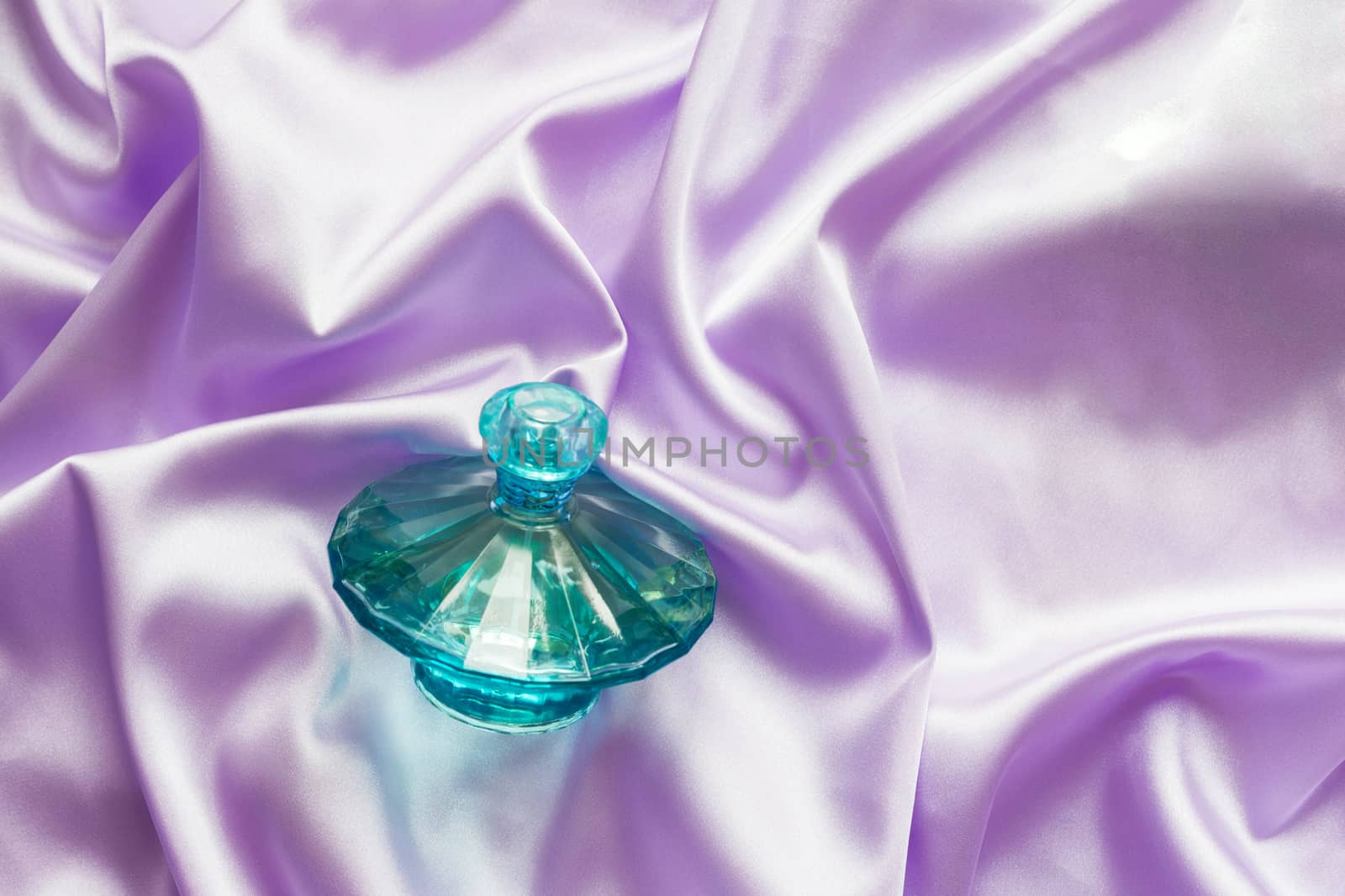 Perfume bottle on lilac silk folded fabric background. Luxery Scent fragrance cosmetic beauty product.