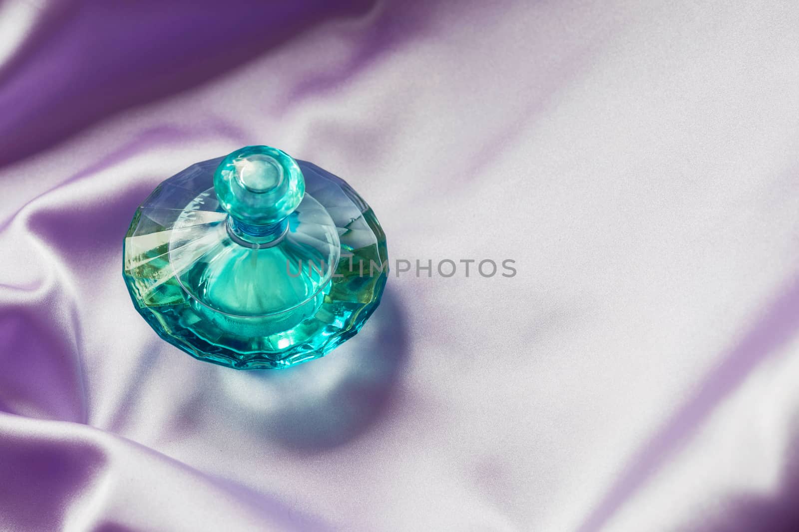 Perfume bottle on lilac silk folded fabric background. Luxery Scent fragrance cosmetic beauty product.