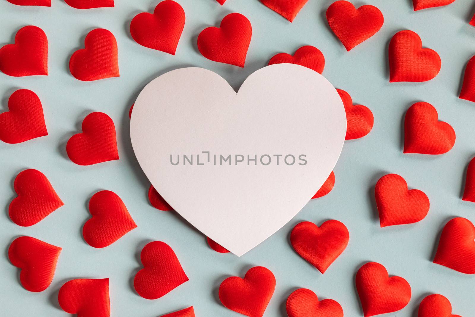 Valentine's day many red silk hearts and white heart shaped card on blue background, love concept