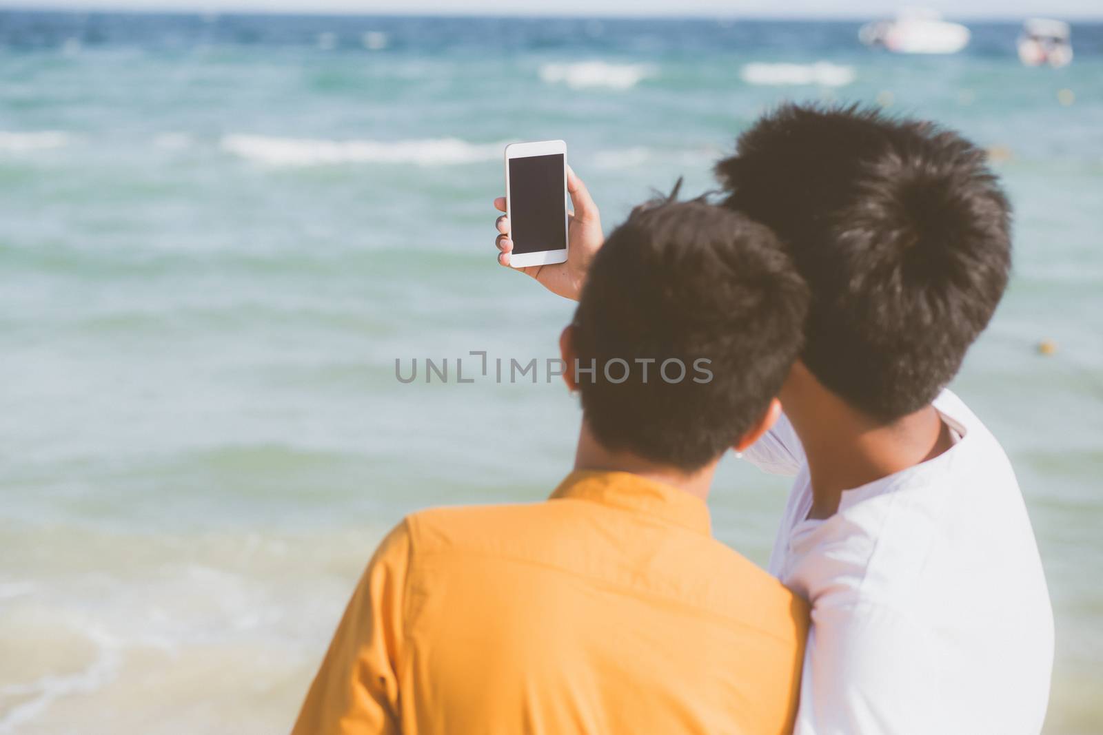 Back view gay portrait young couple smiling taking a selfie photo together with smart mobile phone at beach, LGBT homosexual lover in the vacation at sea, two man going to travel, holiday concept.