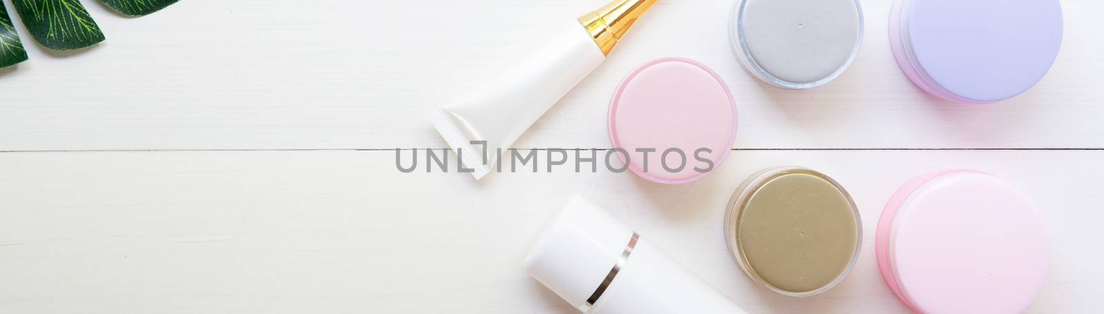 cosmetic and skin care product and green leaves on white wood table, beauty with treatment cream and moisturizing on wooden desk, health and wellness concept, top view, banner website.