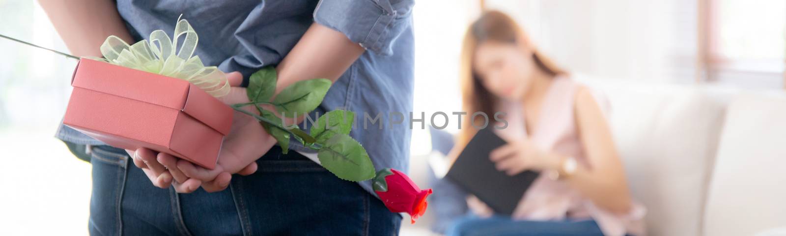 Beautiful young asian couple with man hiding red gift box and rose flower for surprise at home, husband and wife with happy valentine or birthday, married together, family love concept, banner website.