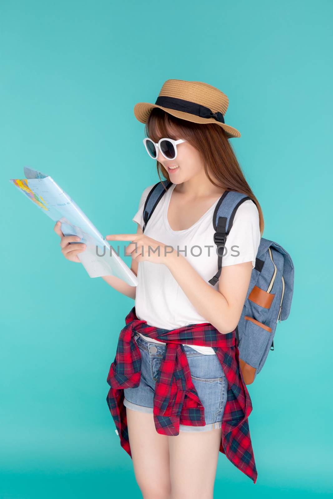 Beautiful happy young asian woman travel looking and pointing a paper map isolated on blue background, asia girl search journey with direction in vacation trip with cheerful for leisure.