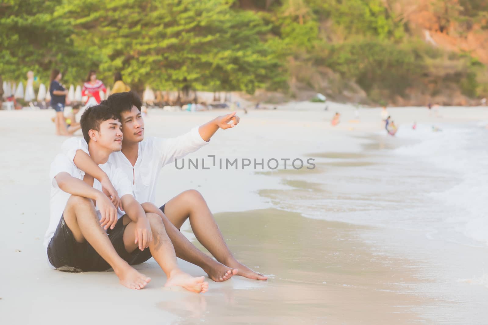 Homosexual portrait young asian couple sitting hug and pointing something together on beach in summer, asia gay going tourism for leisure and relax with happy in vacation at sea, LGBT legal concept.