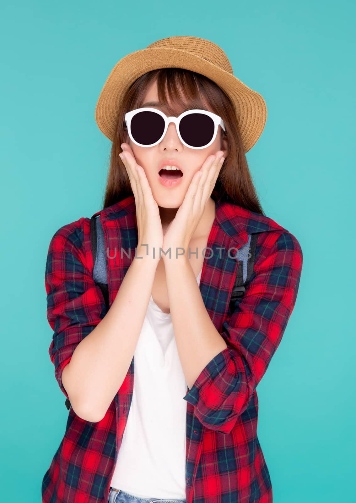 Beautiful portrait young asian woman surprise excited wearing sunglasses and hat travel summer trip isolated on blue background, tourist girl shocked expression and emotion, holiday amazing concept.