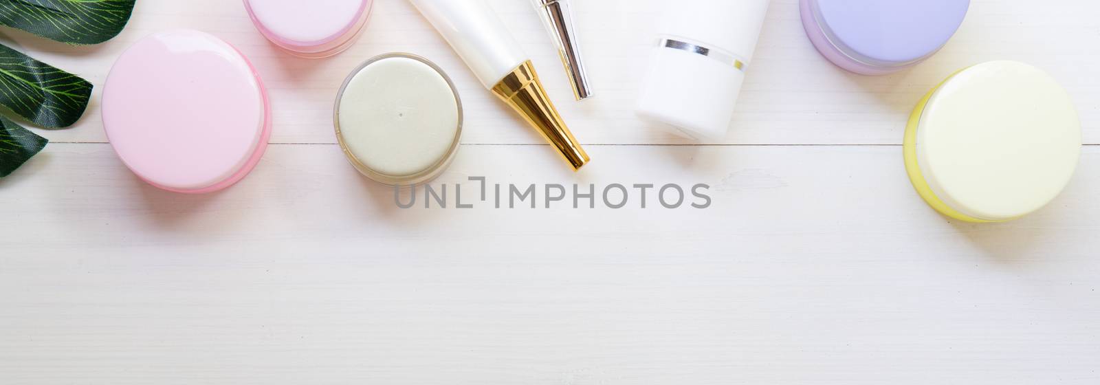 cosmetic and skin care product and green leaves on white wood table, beauty with treatment cream and moisturizing on wooden desk, health and wellness concept, top view, banner website.