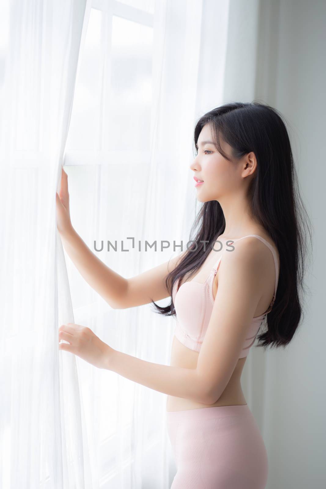 Beautiful young asian woman wake up and walking to window with o by nnudoo