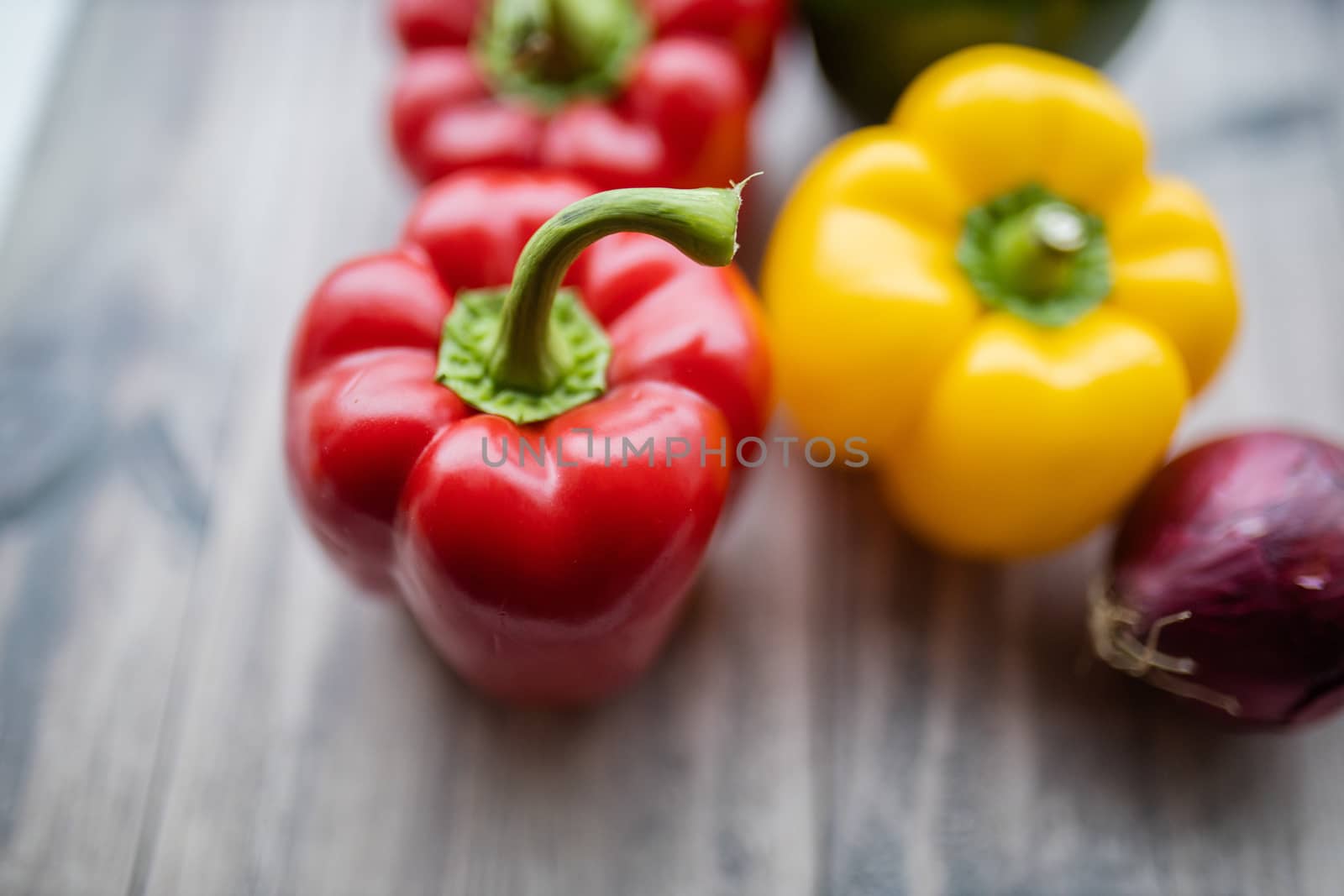 Red and yellow bell peppers and a purple onion up close on a wooden table. Fresh and colorful vegetables on table.Vegan meal ingredients