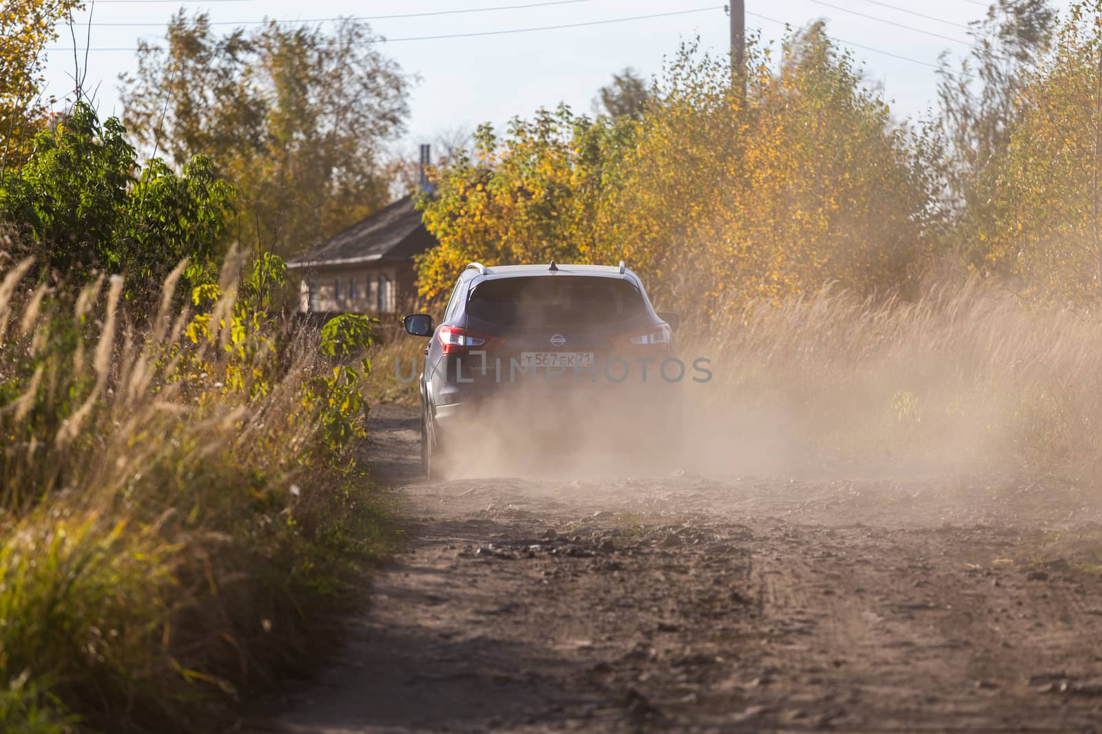 VOLKOVO, RUSSIA - OCTOBER 4, 2020: Blue Nissan Qashqai moving on dirt road with cloud of dust from wheels. Russian country side.