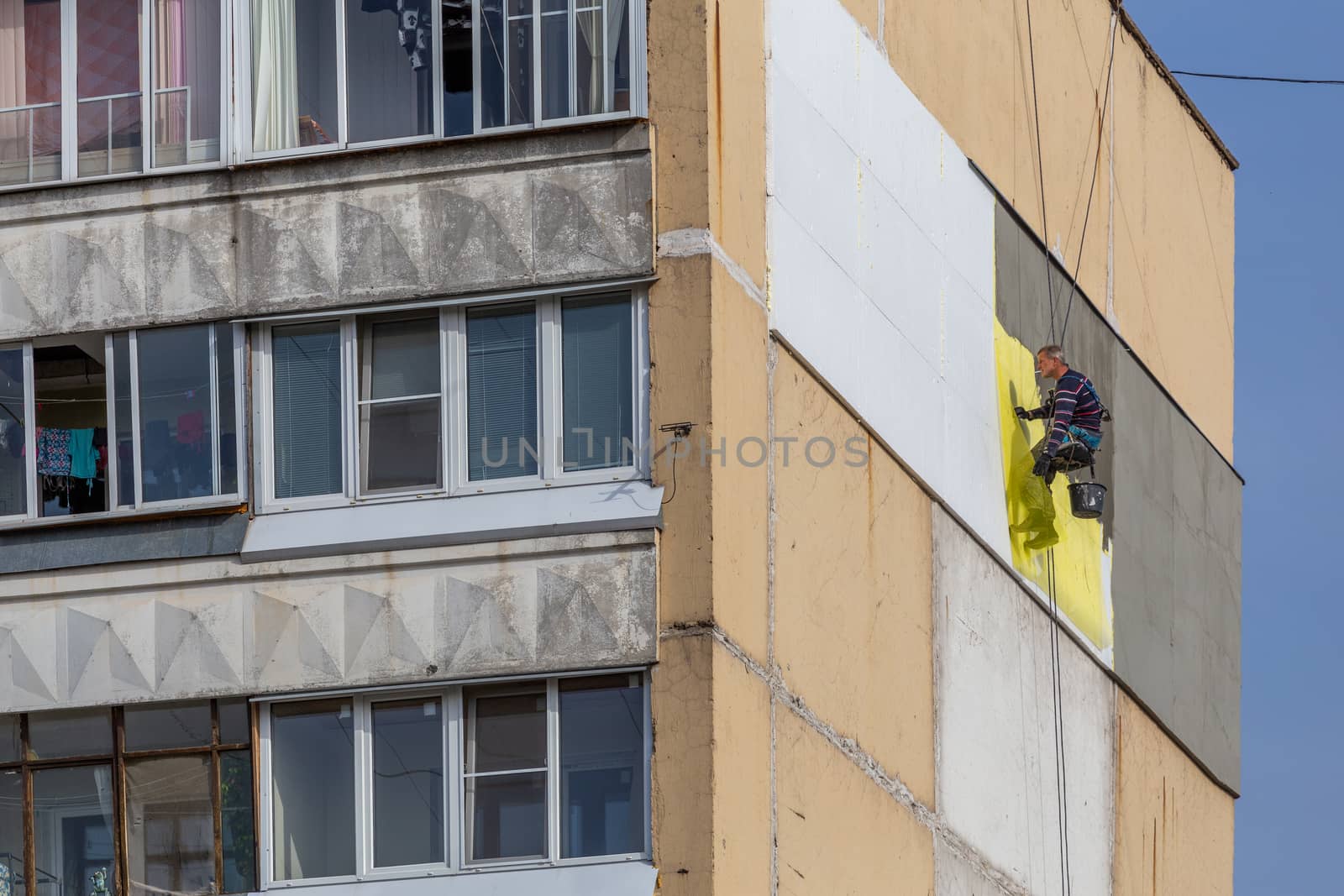 TULA, RUSSIA - OCTOBER 10, 2020: Industrial climber worker applying additional styrofoam insulation on outside wall of nine-storey apartment building at autumn morning daylight. Photo from ground level.