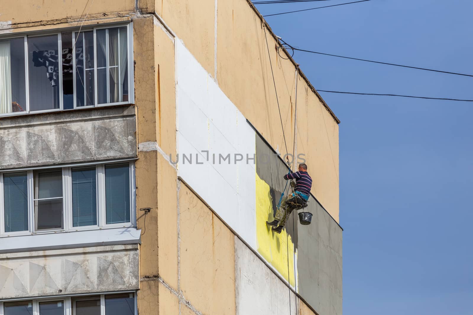 TULA, RUSSIA - OCTOBER 10, 2020: Industrial climber worker applying additional styrofoam insulation on outside wall of nine-storey apartment building at autumn morning daylight. Photo from ground level.