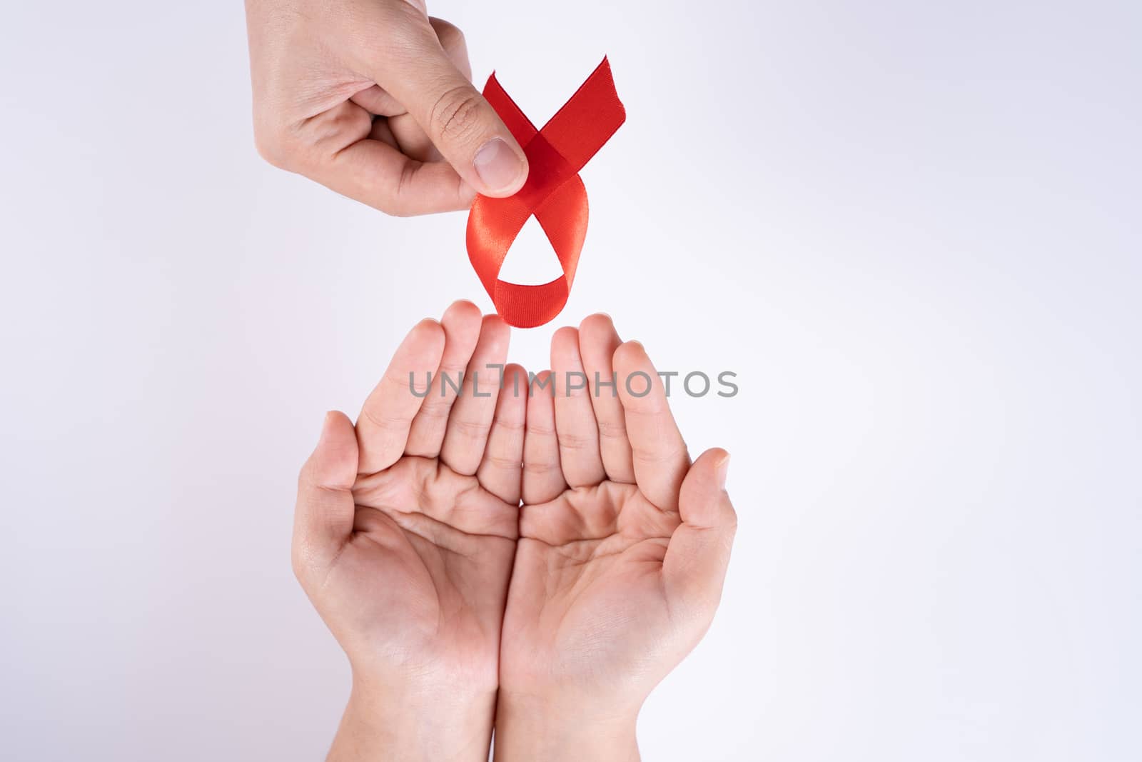 Aids awareness, man and woman hands holding red ribbon on white background with copy space for text. World Aids Day, Healthcare and medical concept.