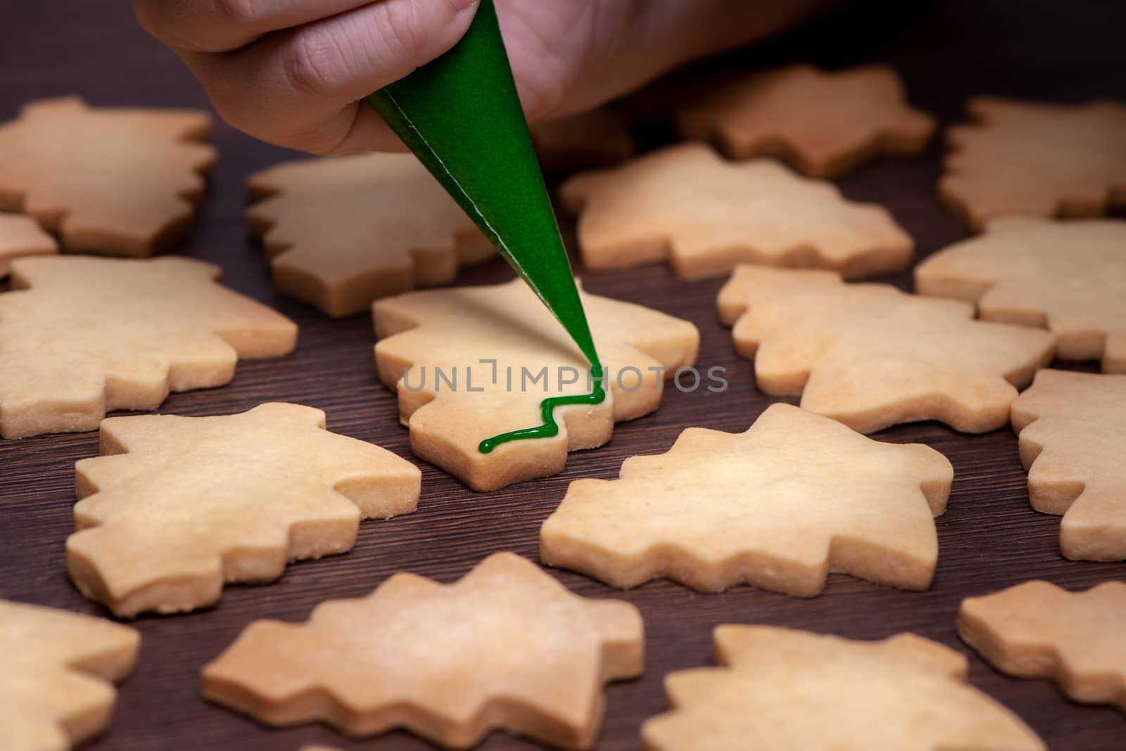 Close up of drawing gingerbread Christmas tree sugar cookie on wooden table background with green icing, concept of holiday celebration.