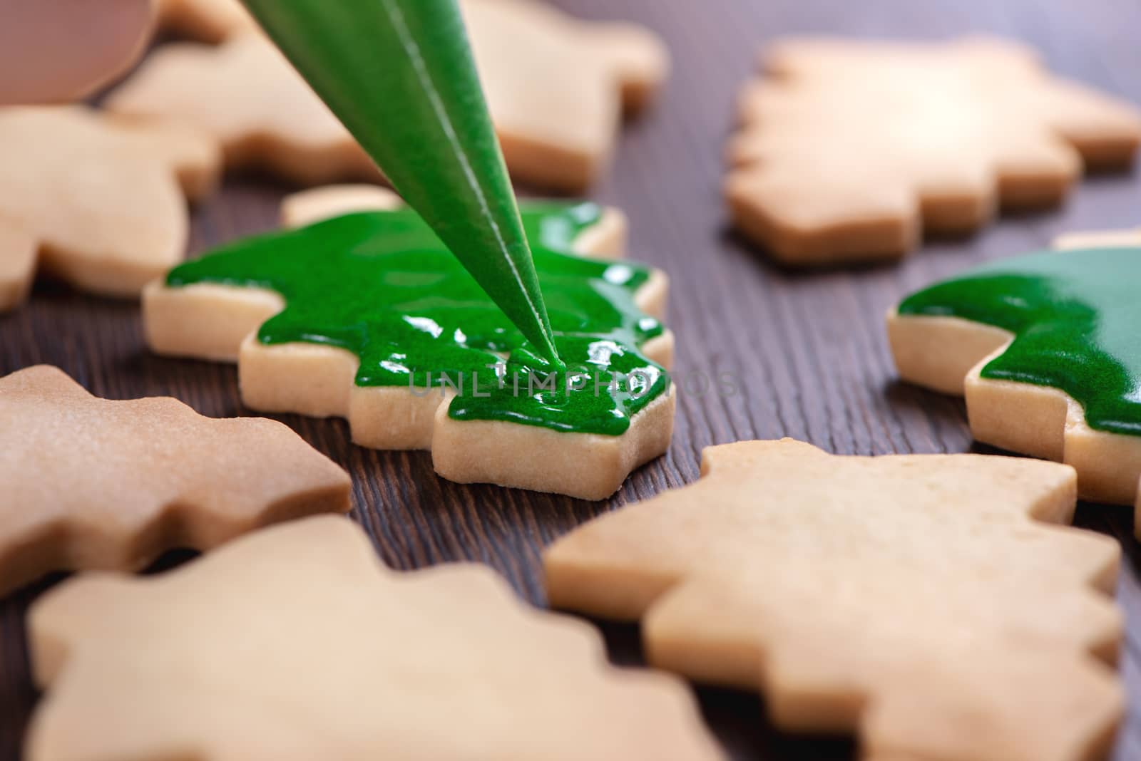 Close up of drawing gingerbread Christmas tree sugar cookie on wooden table background with green icing, concept of holiday celebration.