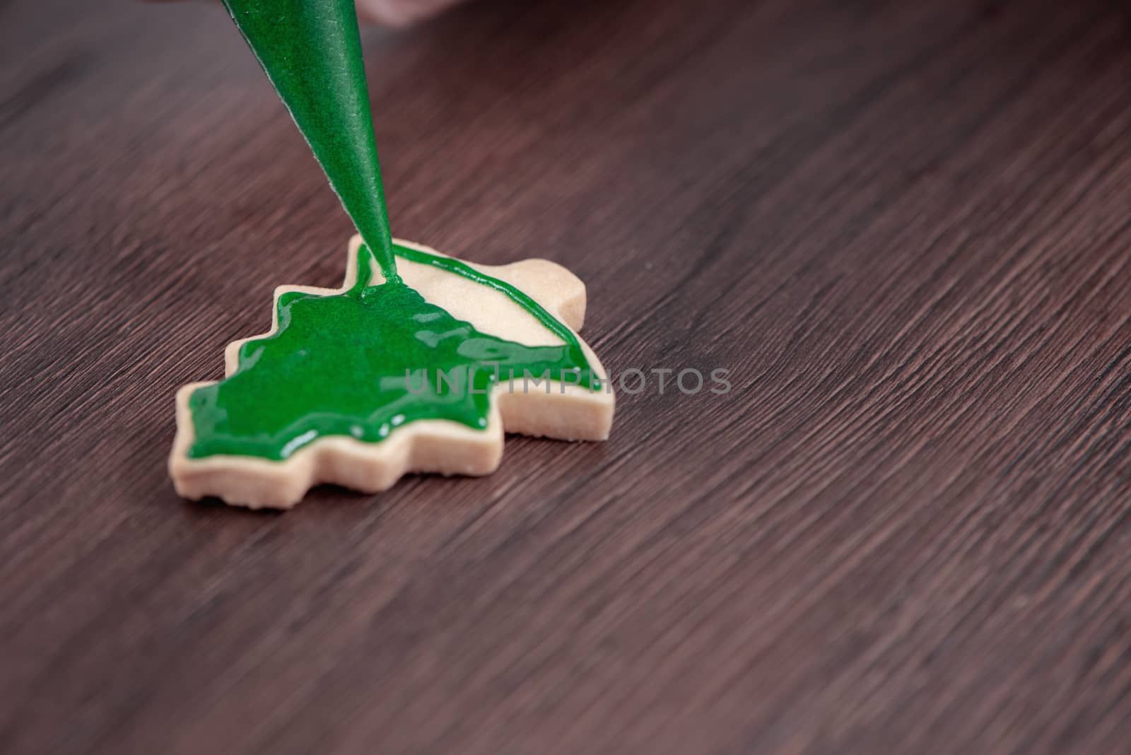 Close up of drawing gingerbread Christmas tree sugar cookie on wooden table background with green icing, concept of holiday celebration.