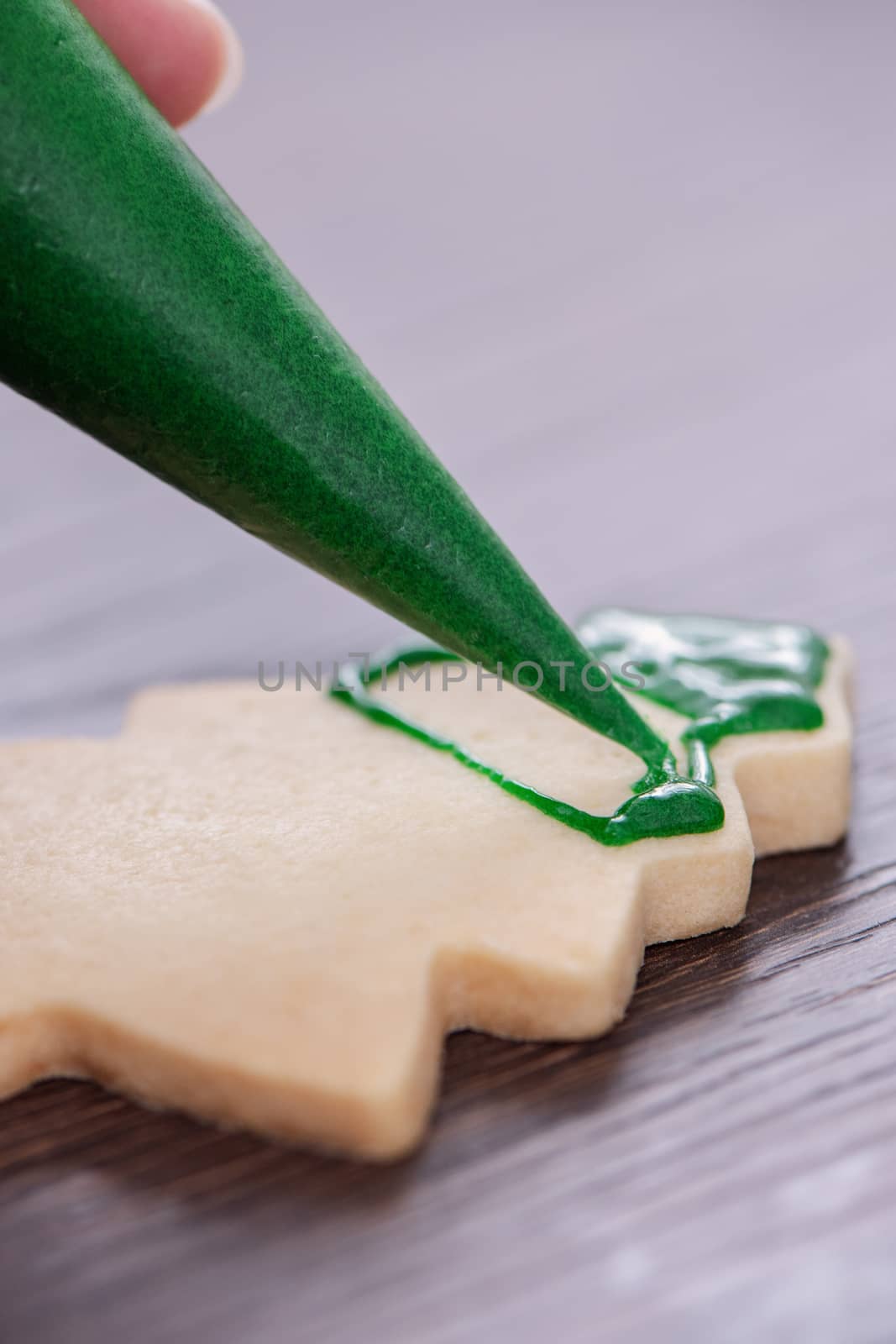 Close up of drawing gingerbread Christmas tree sugar cookie on wooden table background with green icing, concept of holiday celebration.