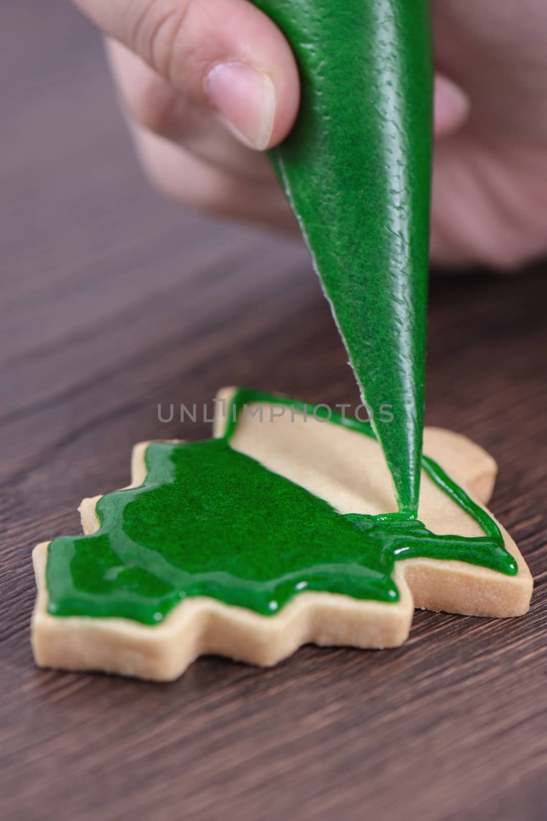 Close up of drawing gingerbread Christmas tree sugar cookie on wooden table background with green icing, concept of holiday celebration.