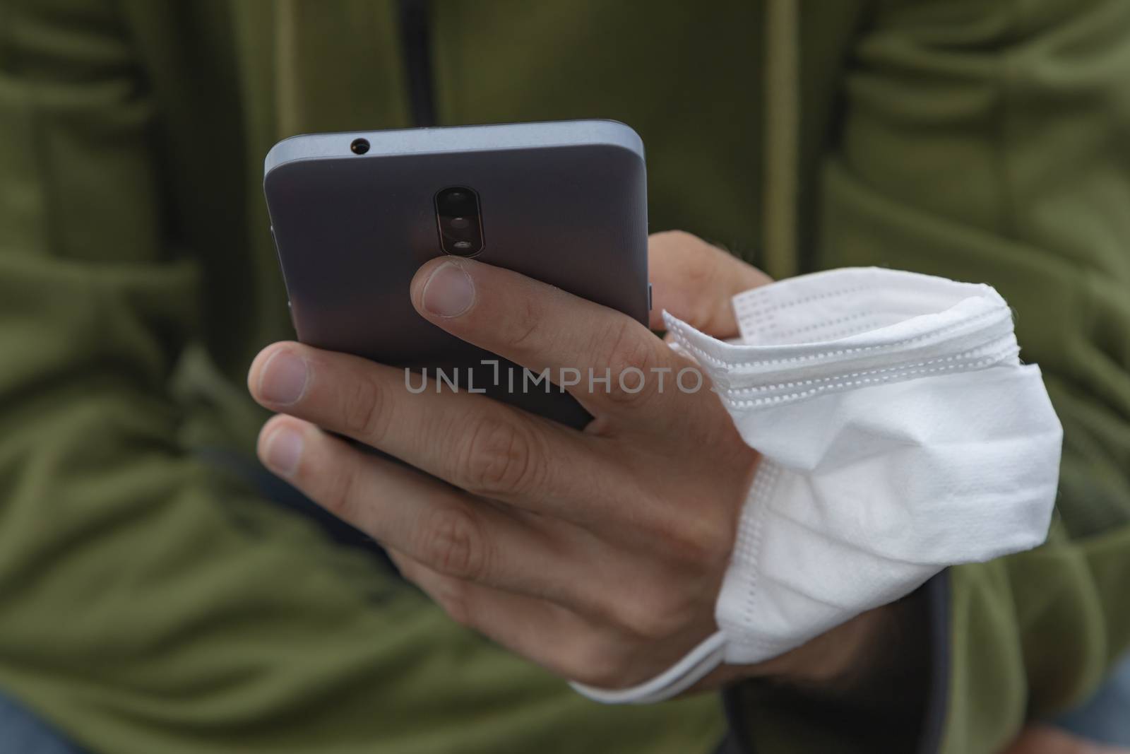 A young man, grabbing a protective face mask, holds a smart mobile phone with his hand, Spain.