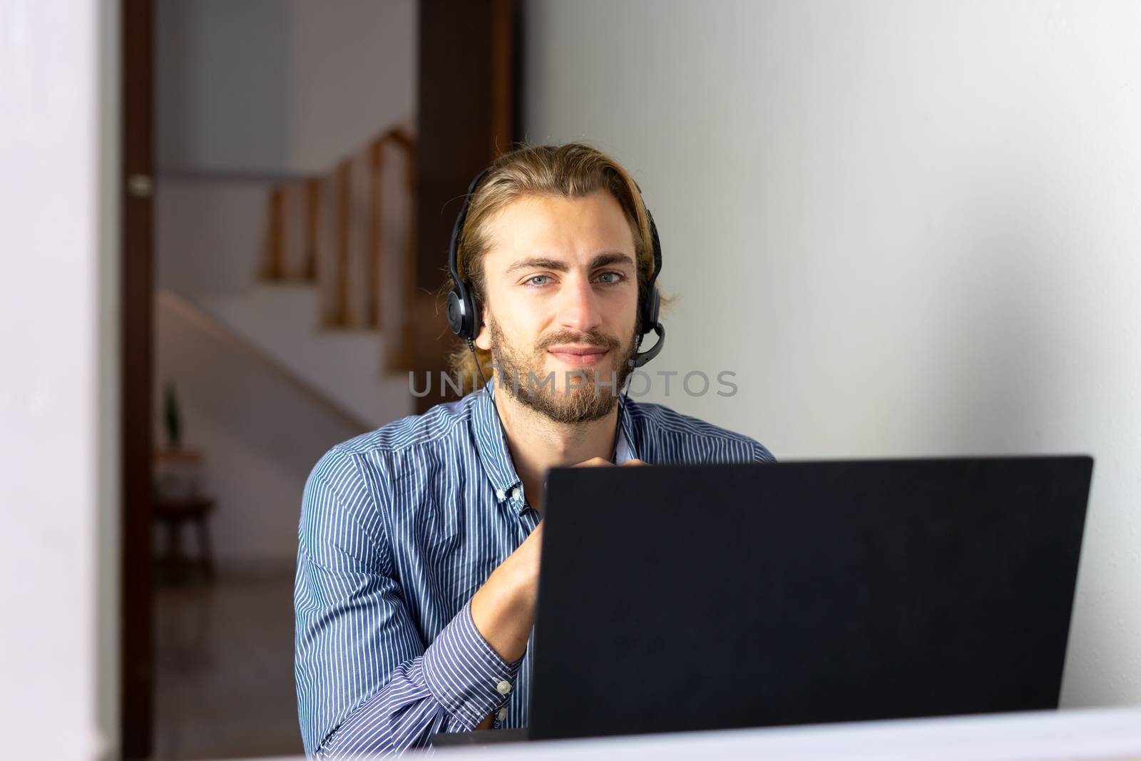 Blond male working from home with headphones using wireless internet on laptop, man call center agent or telemarketer