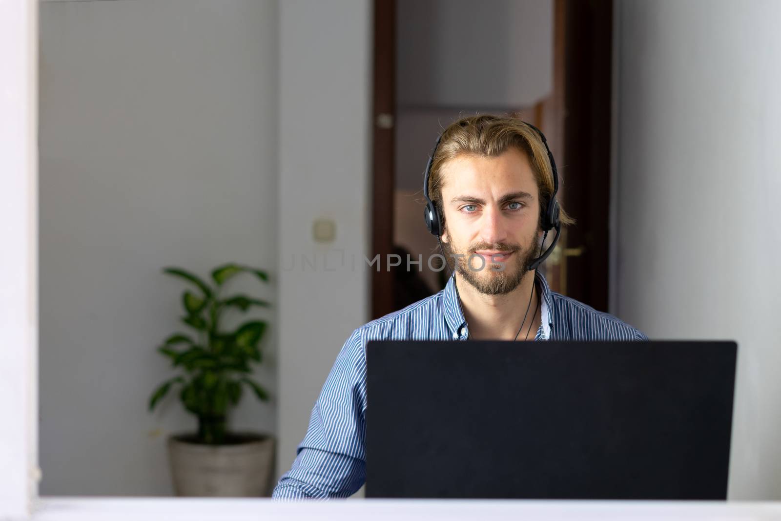 Blond male working from home with headphones using wireless internet on laptop, man call center agent or telemarketer