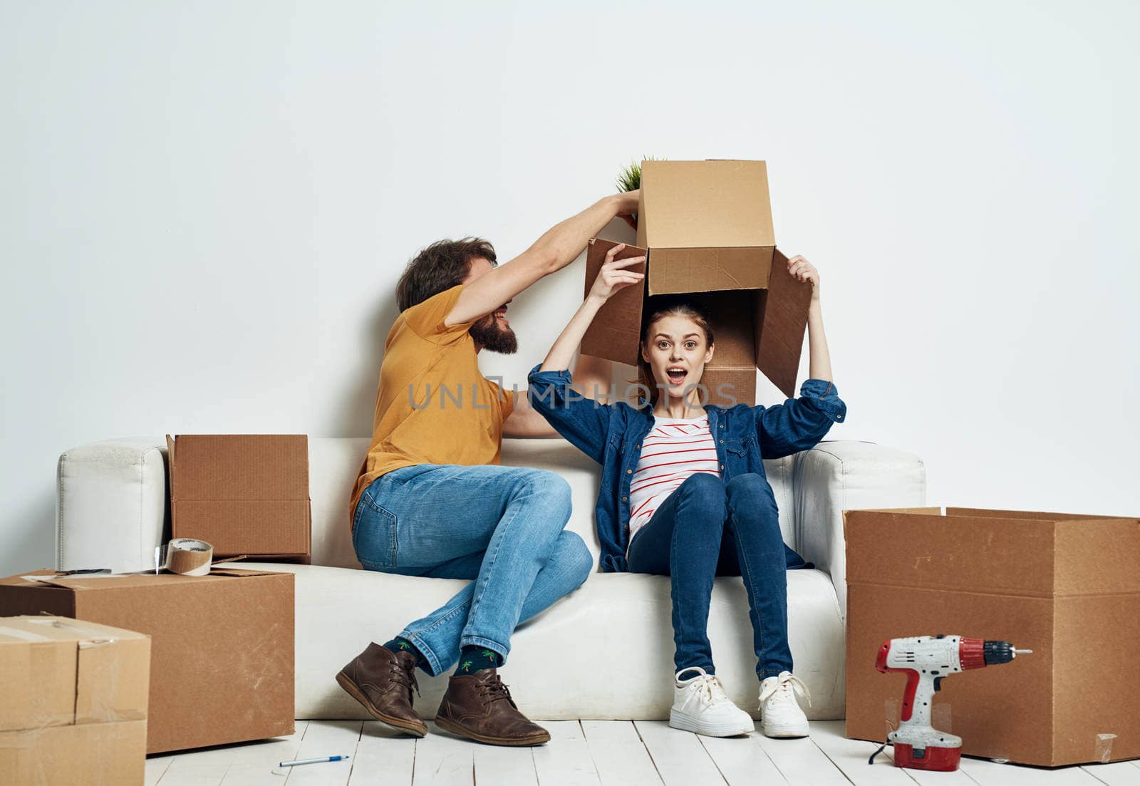 Man and woman sit on white couch boxes with moving lifestyle things by SHOTPRIME