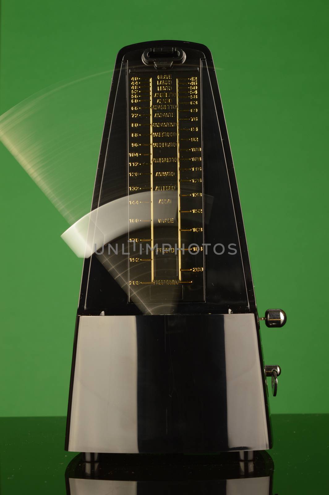 A vertical composition of a working musical metronome over a green background.