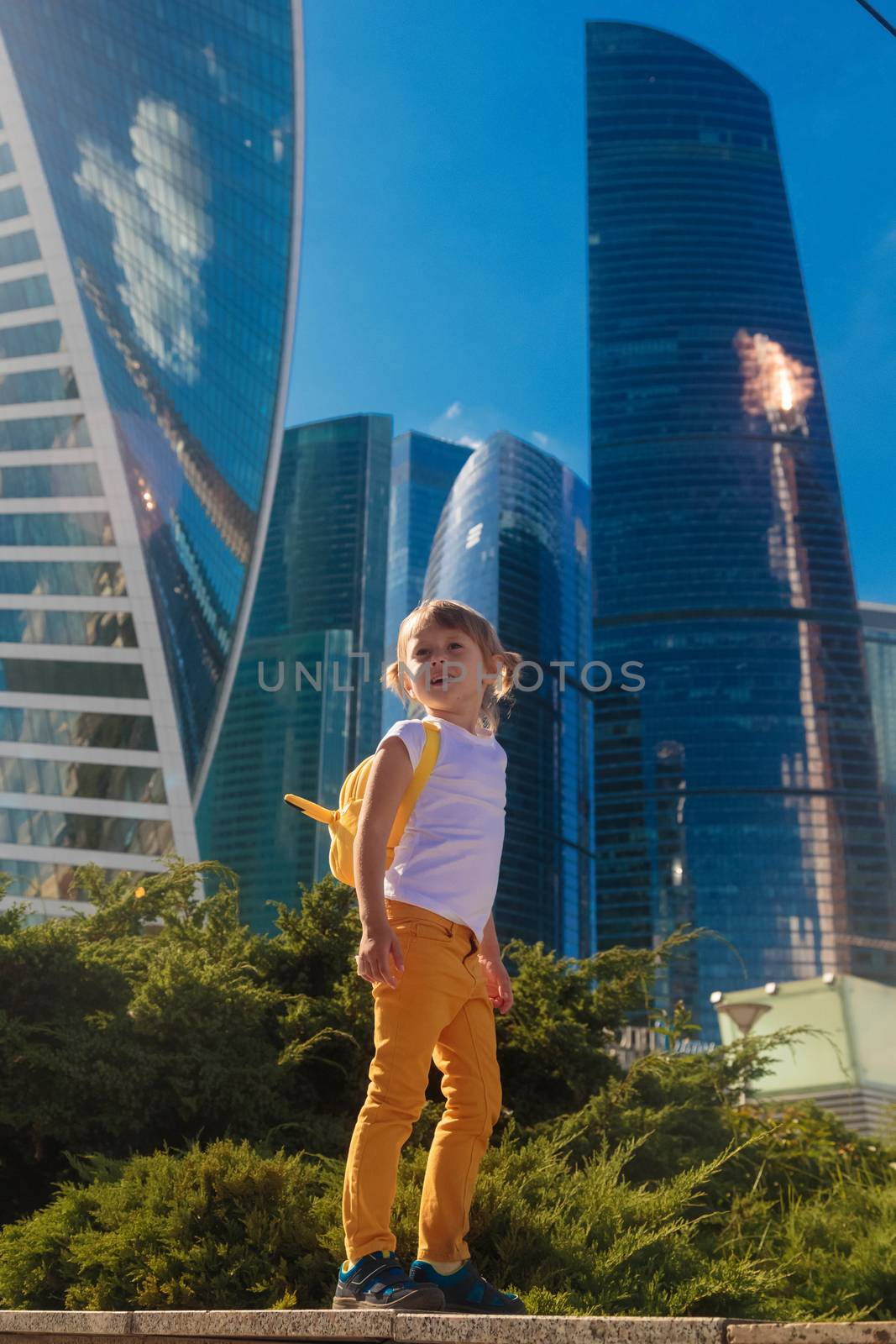A little girl in yellow jeans stands against the background of the skyscrapers by galinasharapova