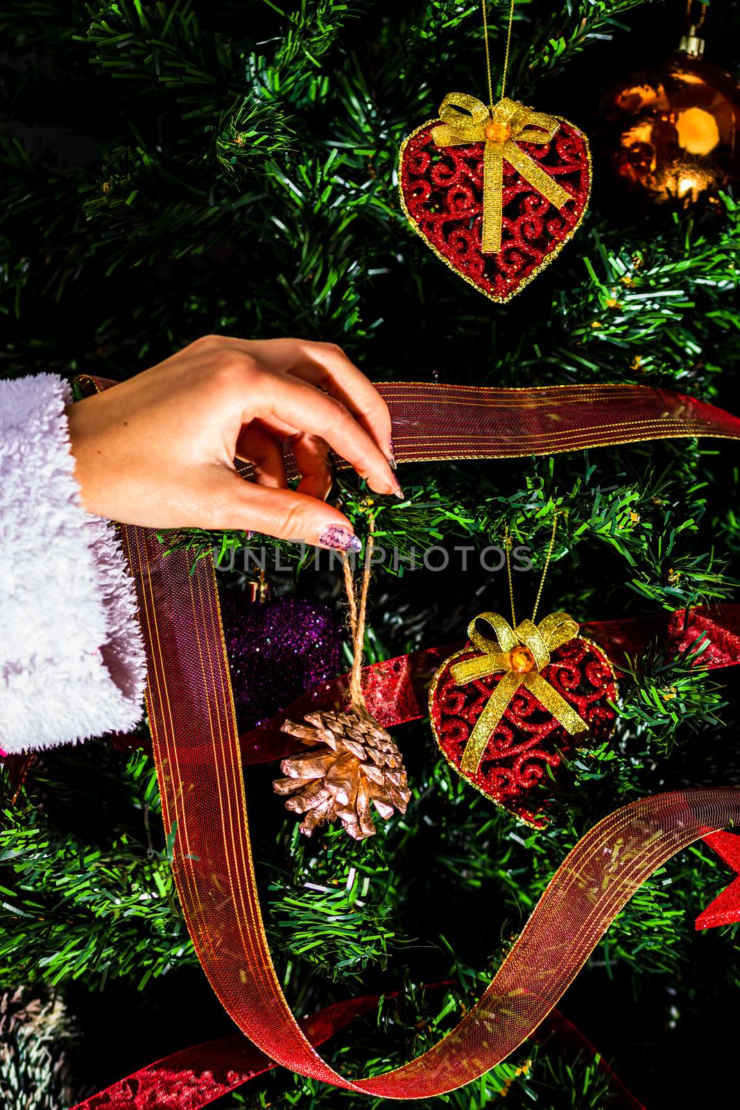 Decorating Christmas tree, hand putting Christmas decorations on fir branches. Christmas hanging decorations.