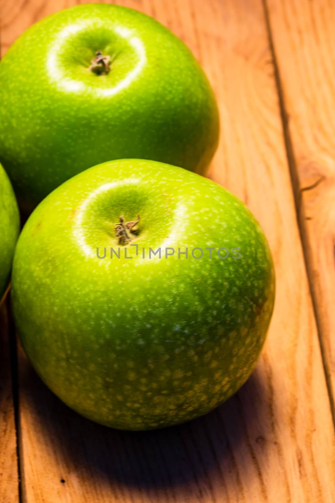 Detail on ripe green apples on wooden table. by vladispas