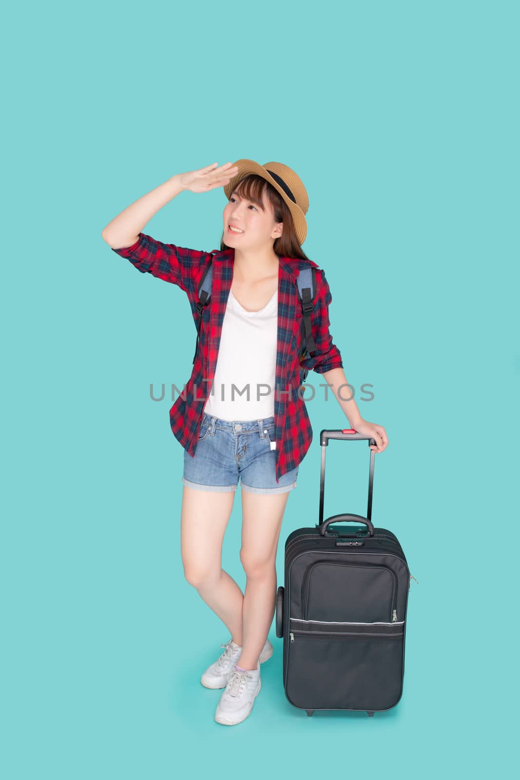 Beautiful young asian woman pulling suitcase isolated on blue ba by nnudoo