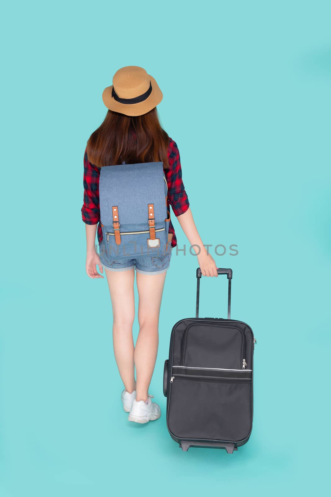 Back view beautiful young asian woman pulling suitcase isolated on blue background, asia girl having expression is cheerful holding luggage walking in vacation with excited, journey and travel concept.