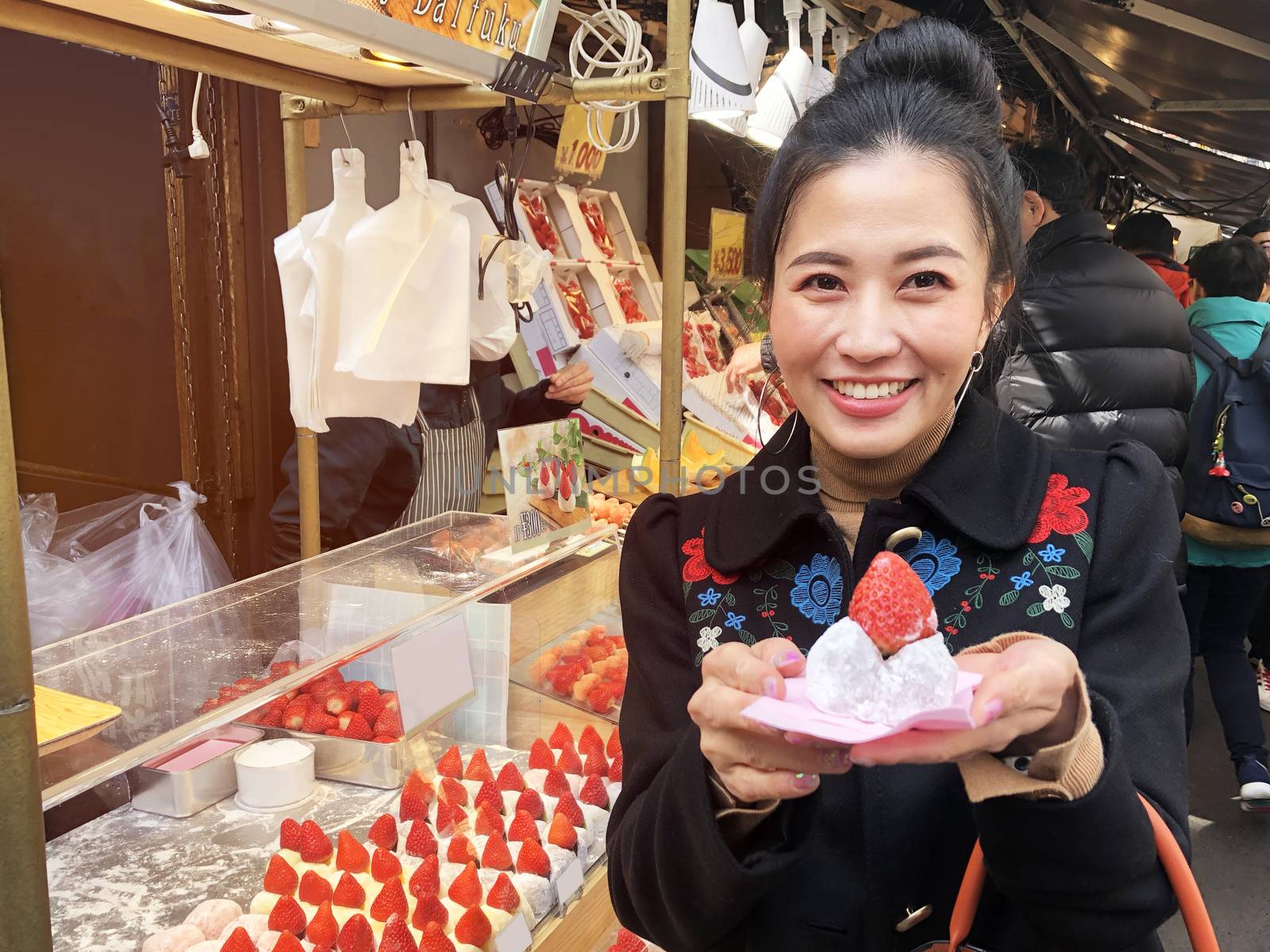 Tourist woman showing street food strawberry Daifuku, Strawberry Mochi at Tsukiji Fish Market in Tokyo.

