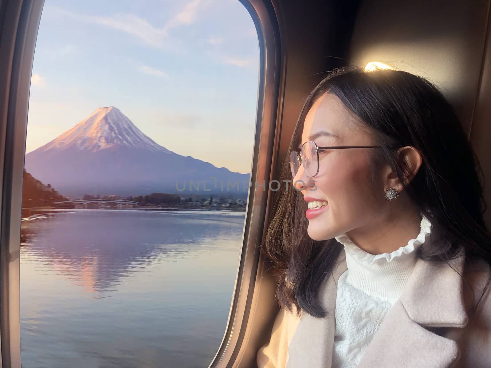 Young woman traveling by the train from sitting near the window and looking view of mountain Fuji in sunrise ,Japan