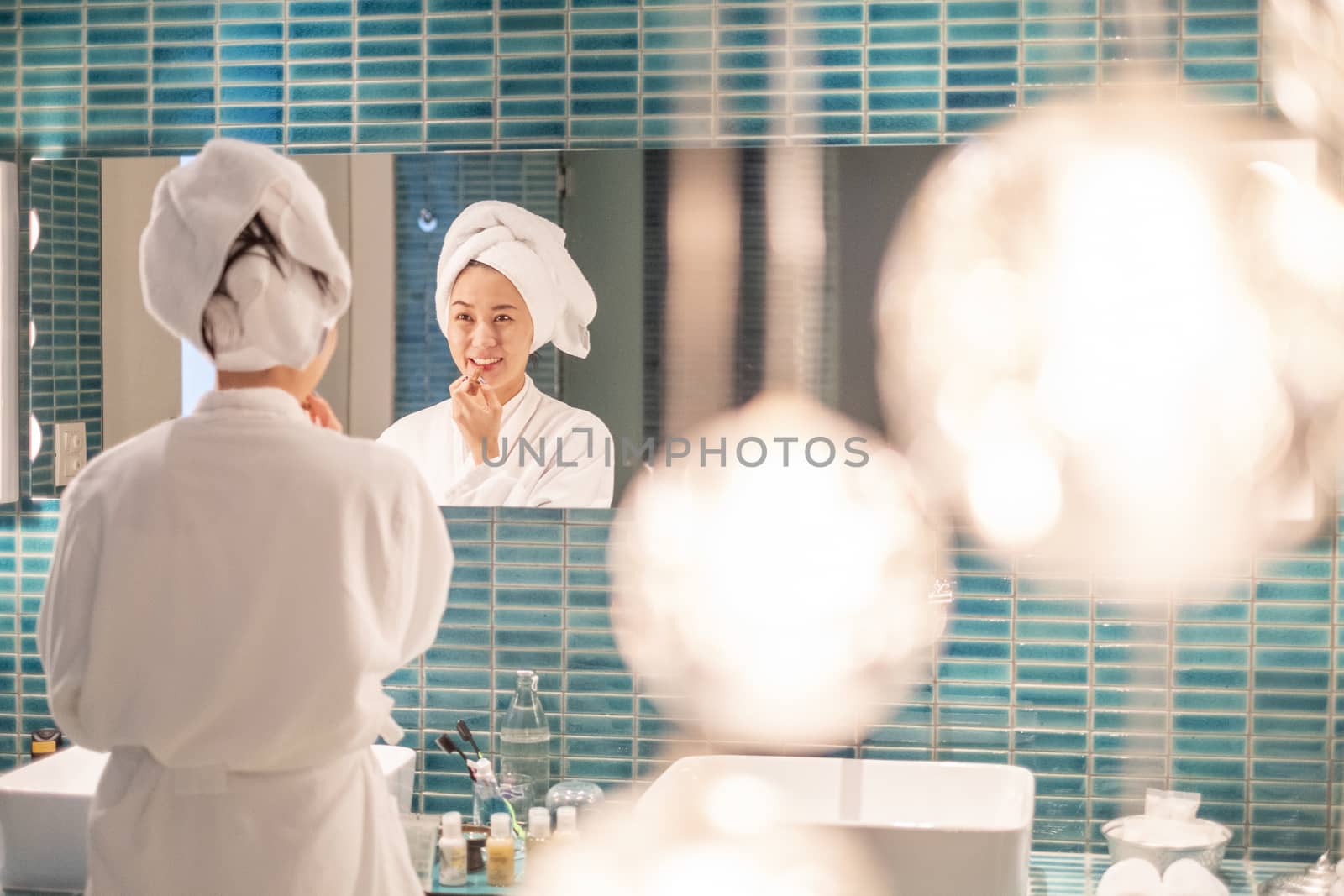 Young woman putting on makeup after shower  by Surasak