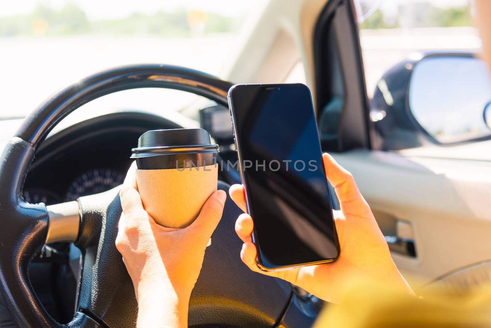 Asian woman drinking hot coffee takeaway cup inside a car and using smartphone blank screen while driving the car in the morning during going to work on highway, Transportation and vehicle concept