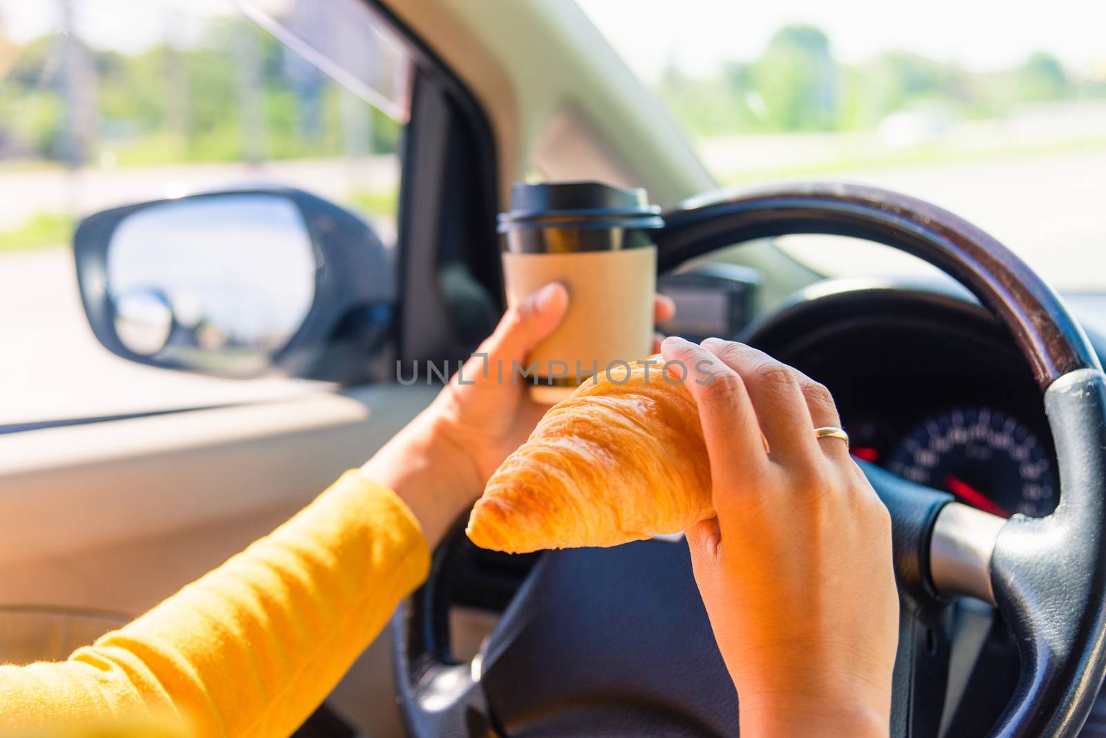 Asian woman eating food fastfood and drink coffee while driving the car in the morning during going to work on highway road, Transportation and vehicle concept