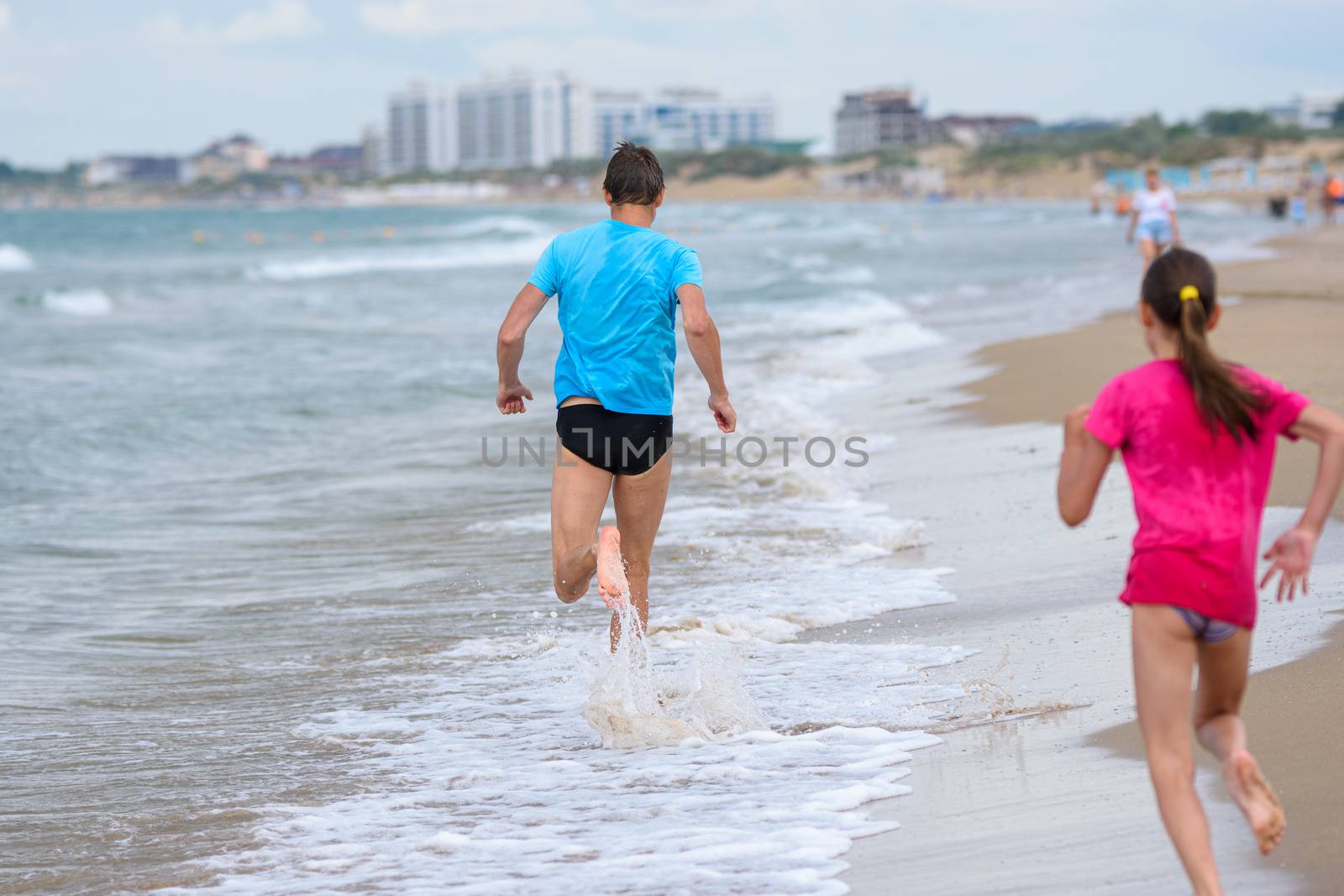 A man runs along the beach, a girl runs after him, rear view