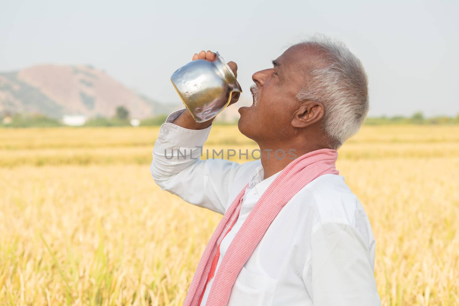 Thirsty Indian farmer drinking water from steel tumbler or Chambu on hot sunny day at agriculture field by lakshmiprasad.maski@gmai.com