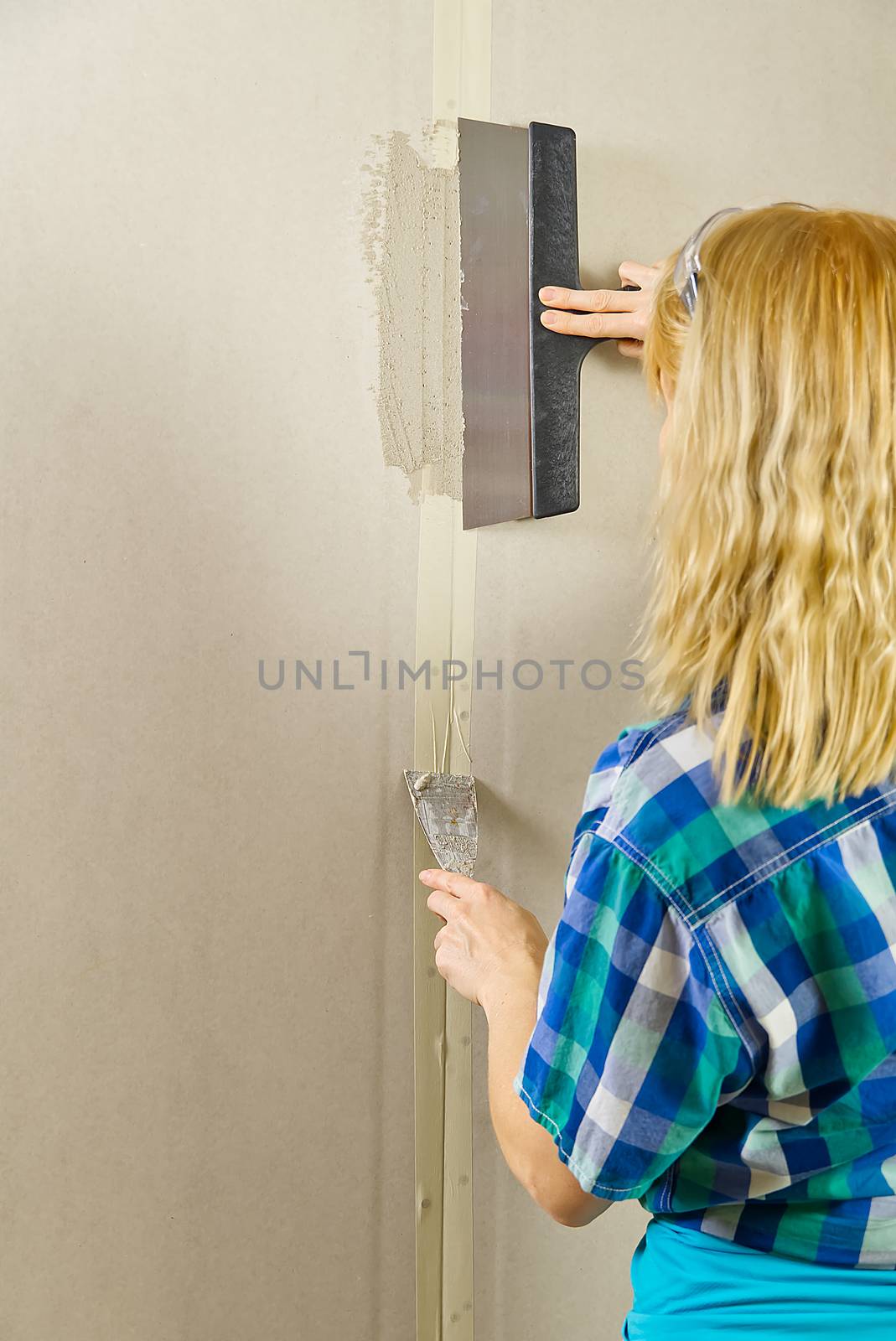 Woman putty plaster. Builder female indoor worker plastering wall with spatula trowel tool. by PhotoTime