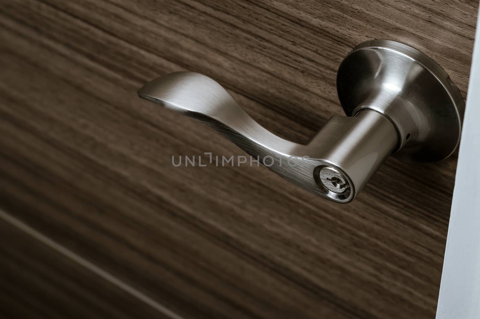 stainless steel door knob or handle with keyhole on wooden door, wave style lever handle front door knob with lock, modern interior design concept, shallow depth of field