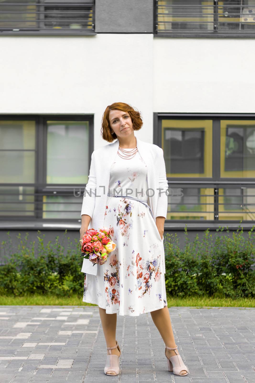 Woman in white dress with bouquet of flowers. Portret. Against backdrop of city house. by Essffes