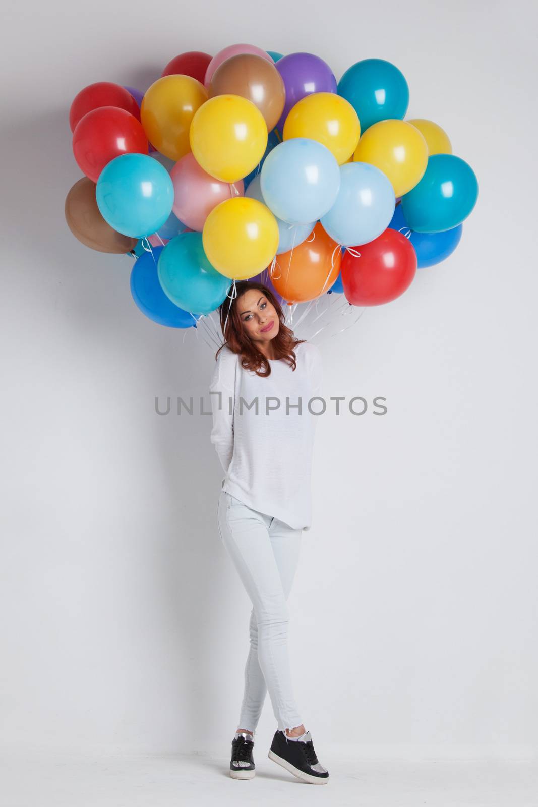 Young pretty woman in white clothes with colored balloons on white background with copy space for text