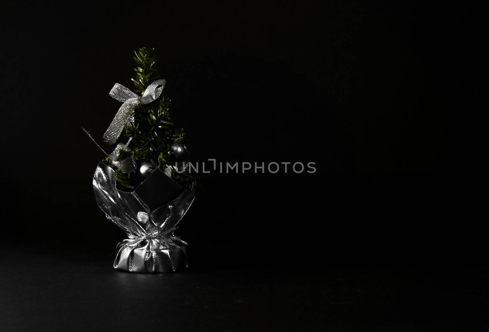 Small Christmas tree in a bag with decorations. Table accessory with silver decor. Christmas tree on black background for greeting cards