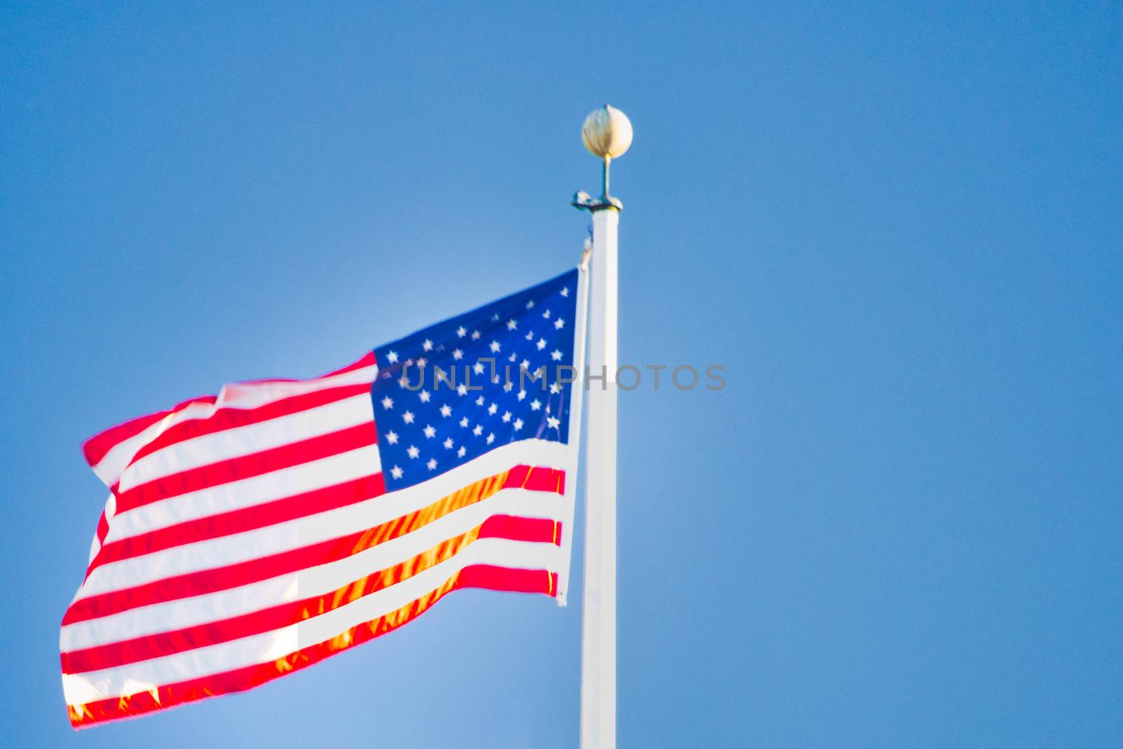 American flag with pole and copy space waving in the wind. Copy Space provided. Bright blue sky.