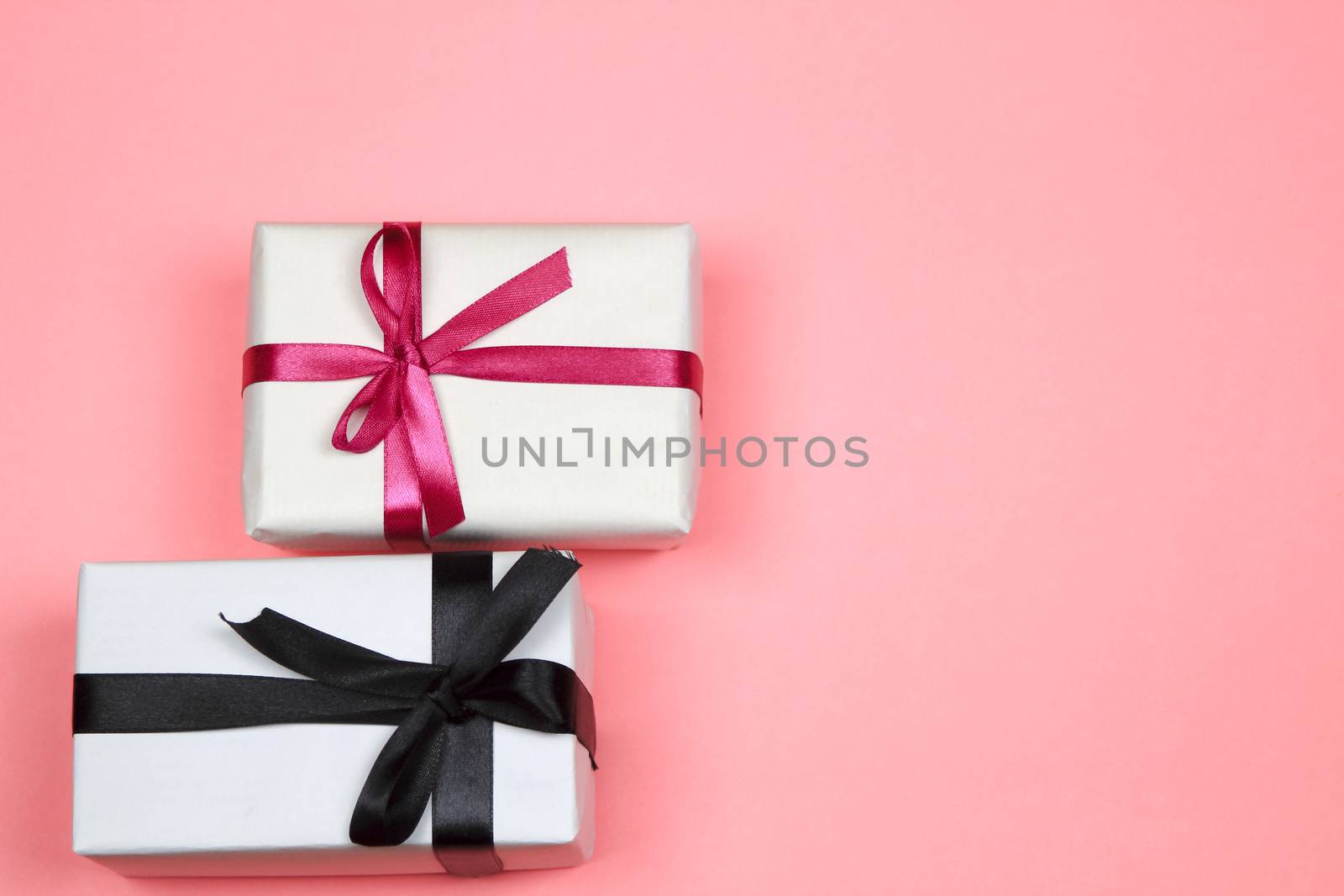Gifts wrapped with white paper and pink and black bows on pink background