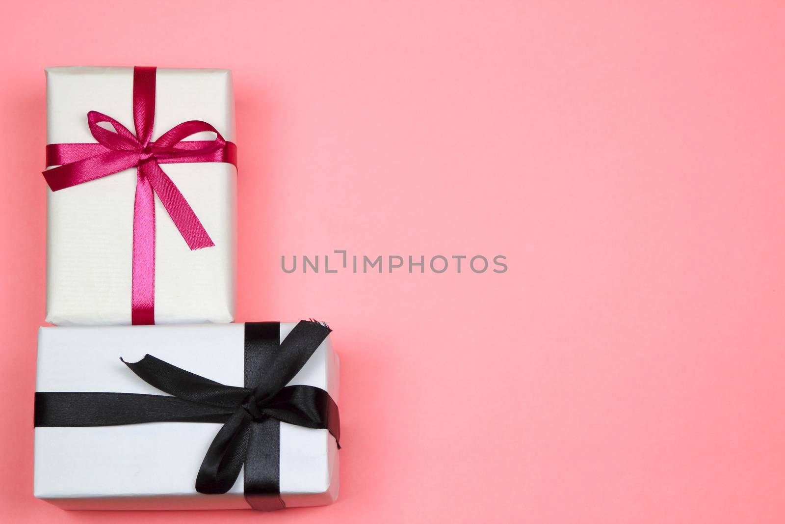 Gifts wrapped with white paper and pink and black bows on pink background
