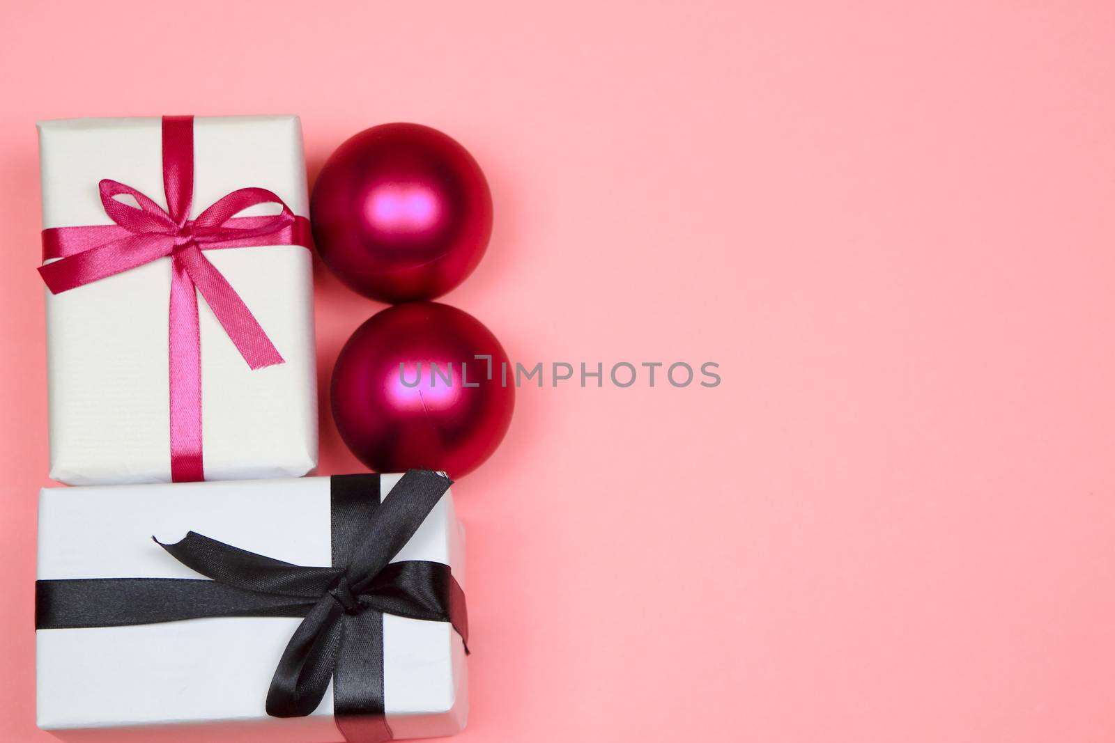 Gift wrapped with white paper and pink bow next to Christmas decoration on pink background