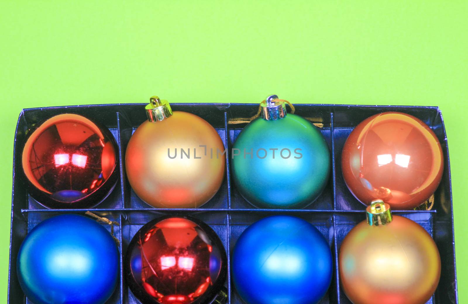 Box of multicolor Christmas balls on green background